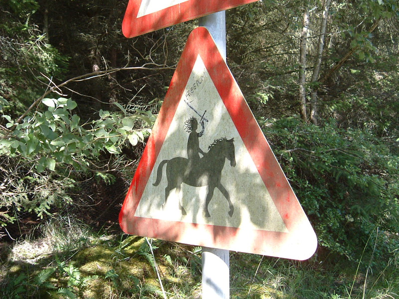 A road sign warning of people on horses, on which someone has added a sword in the hand of the rider